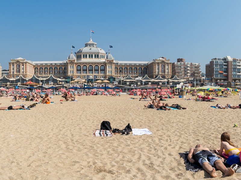 Zonnig strand met badgasten voor het historische Kurhaus in Scheveningen.